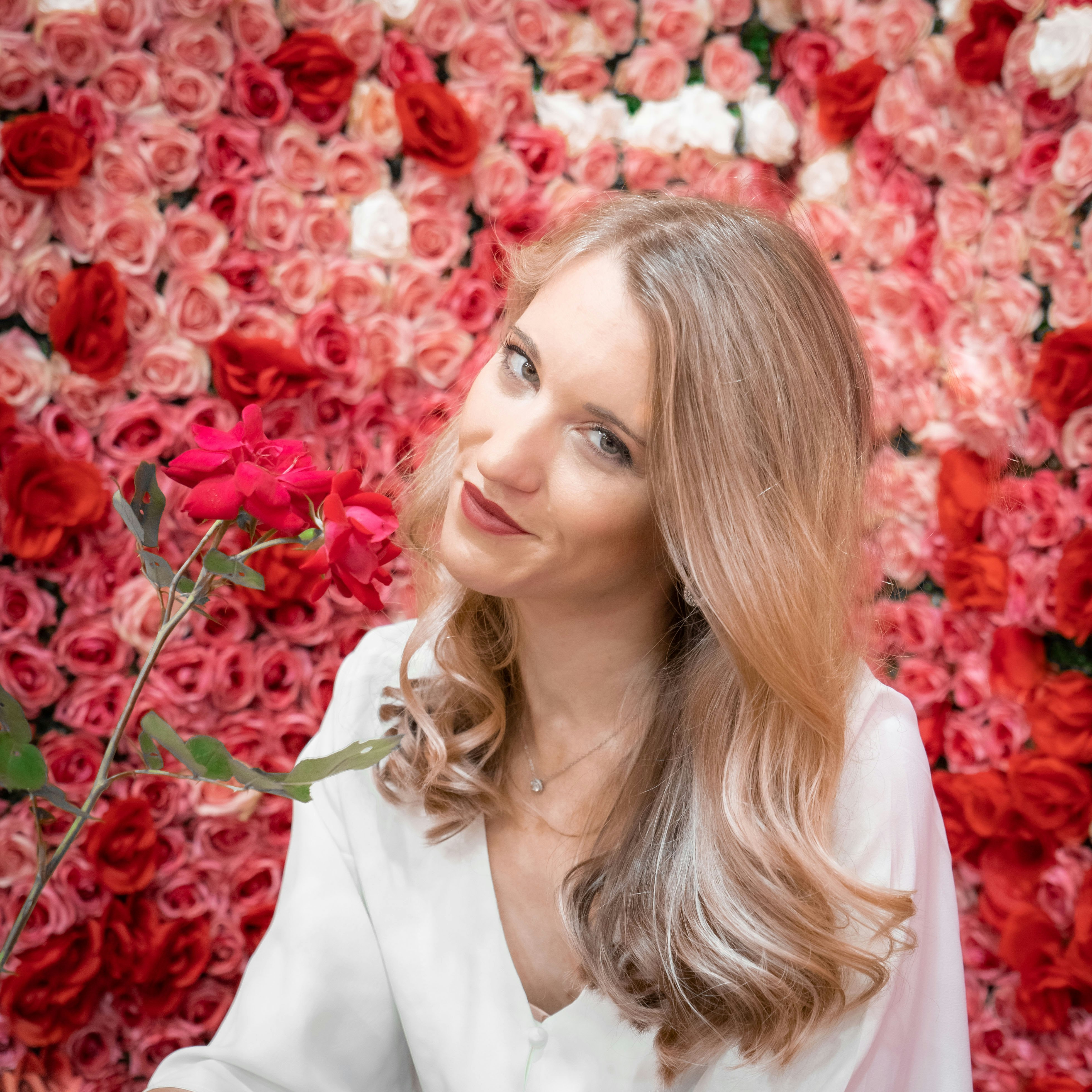 woman in white blazer standing near red flowers